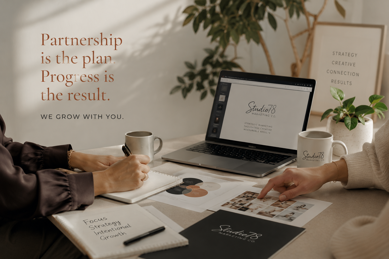 A working session with hands pointing to printed brand strategy materials, a laptop showing Studio78 branding, notebooks, and coffee mugs on a warm, natural desk